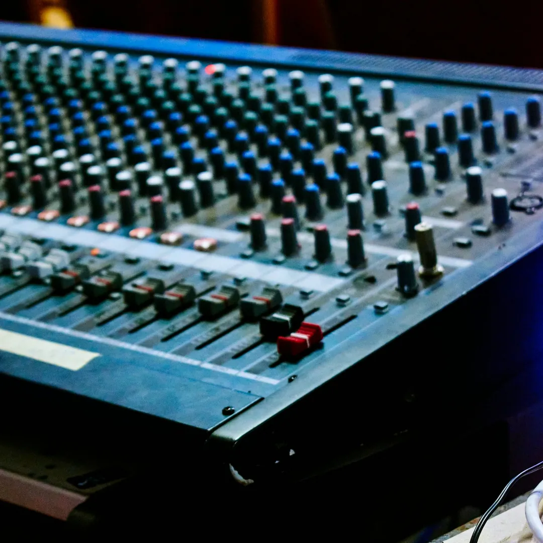 Primer plano de una consola de mezcla con faders, perillas y botones iluminados en la sala de control de un estudio
